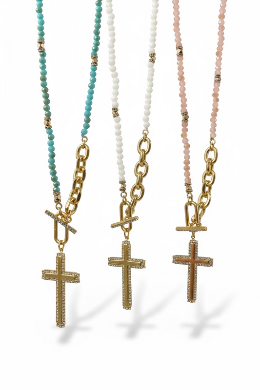 Three gold cross necklaces with beaded chains on a wooden surface.