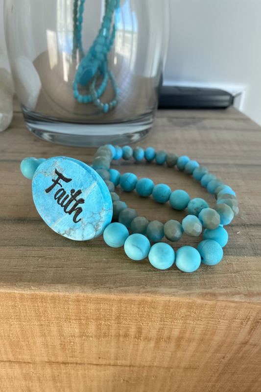 Turquoise beaded bracelet with 'Faith' charm on a wooden surface